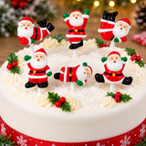 Six Christmas Santa Claus cake toppers decorated in red, green, white, and black, arranged on a white frosted round cake with festive decorations.
