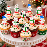A group of decorated cupcakes arranged on a white cake stand in a festive holiday setting. The cupcakes have white frosting topped with snowman figurines, red and green sprinkles, and red, white, and green patterned liners.