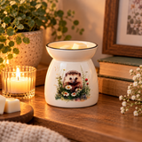 A ceramic wax warmer with a printed hedgehog and wildflowers design, set on a wooden table next to a lit candle, books, and greenery.
