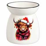 A white ceramic oil burner or scented candle holder with a black rim, featuring a printed illustration of a Highland cow wearing a red Santa hat and plaid scarf on a white background.