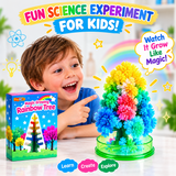A young boy smiling and pointing at a colorful rainbow crystal tree made from the Magic Growing Rainbow Tree kit, with its blue retail box shown on the left. The scene is decorated with playful graphics, including a rainbow, stars, and text overlays that read 'FUN SCIENCE EXPERIMENT FOR KIDS!' and 'Watch It Grow Like Magic!'.