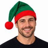 A smiling man wearing a festive green and red elf hat with a red pom-pom, isolated on a solid black background.