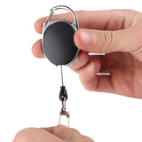 Hand holding a retractable keychain with a black circle and metal clip on a white background