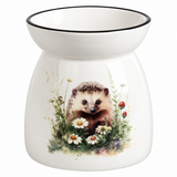 A white ceramic oil burner or scented candle holder with a black rim, featuring a printed illustration of a hedgehog surrounded by daisies, clovers, and red berries on a white background.