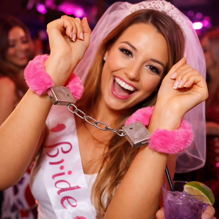 Woman in a bachelorette party scenario with handcuffs and 'Bride' sash, holding a drink.