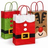 Three Christmas-themed paper gift bags with handles, arranged in front of a white background. The left bag is green with red and black accents resembling an elf's body.