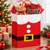 A red Santa Claus-themed gift bag filled with wrapped presents, a teddy bear, candy canes, and gift boxes, set on a wooden table with a decorated Christmas tree in the background.