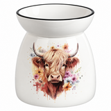 A white ceramic oil burner or scented candle holder with a black rim, featuring a colorful watercolor illustration of a Highland cow surrounded by flowers on the front.