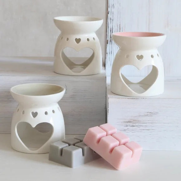 Set of white ceramic heart-shaped candle holders with a pink soap bar on a light wooden surface.