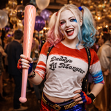 Person dressed as Harley Quinn holding a Inflatable baseball bat in a party setting with balloons.