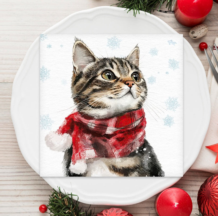 Napkin with a cat wearing a red scarf design on a white plate with Christmas decorations.