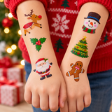 A person wearing a red Christmas sweater shows two temporary arm and wrist decals with festive holiday designs, including a reindeer, holly, Santa, snowman, Christmas tree, and gingerbread man, against a blurred Christmas tree and gift background.