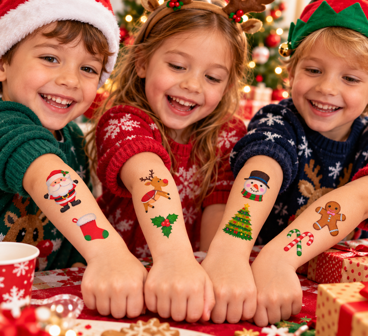 Three children smiling at a Christmas table, each with a colorful holiday temporary tattoo on their forearm. The tattoos include Santa Claus, a reindeer, a snowman, a Christmas tree, and a gingerbread cookie.