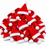 A pile of small red Santa Claus hats with white trim and white pom-poms, photographed on a plain white background.
