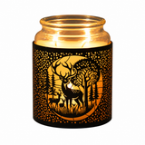 A lit candle in a clear glass jar with a black decorative sleeve featuring a warm orange forest and deer silhouette design, shown on a plain white background.