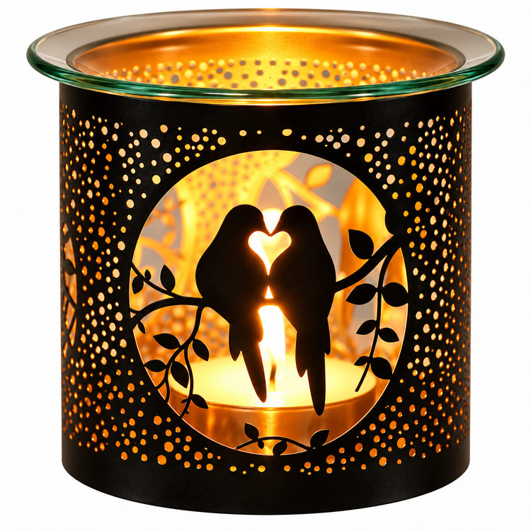 A black metal candle warmer with a glass rim, featuring a cutout design of two birds on a branch with a heart-shaped flame in the center, glowing warmly against a white background.