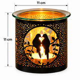 Black metal candle holder with laser-cut bird and heart silhouette design, illuminated with warm orange light inside. Features dimension annotations showing 11 cm height and width on a white background.