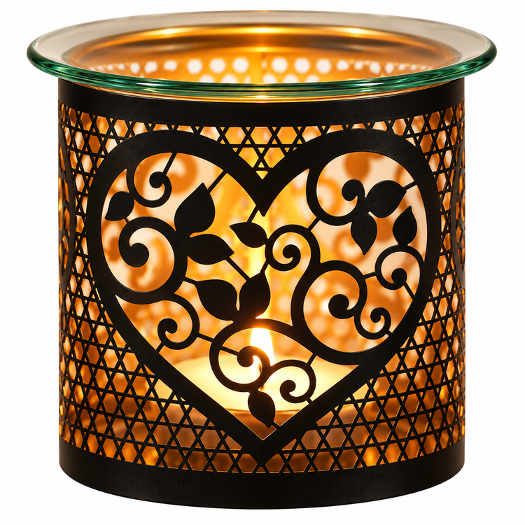 A cylindrical glass and metal candle holder with a black heart-shaped cutout and leaf scroll pattern, glowing with a warm orange candlelight inside on a white background.