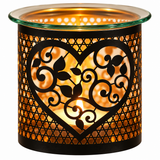 A cylindrical glass and metal candle holder with a black heart-shaped cutout and leaf scroll pattern, glowing with a warm orange candlelight inside on a white background.