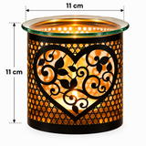 A black metal candle holder with a heart-shaped cutout and scrollwork pattern, illuminated from within to show warm orange light. The top rim is clear glass, and the image includes dimension lines indicating a height of 11 cm and a diameter of 11 cm.