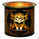 A black metal candle holder with a glowing warm interior, featuring a cartoon Highland cow illustration and a border of small cutout dots on the front, with a clear glass rim at the top.