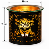 A black cylindrical candle holder or diffuser with a cartoon Highland cow design and orange-gold cutout dots, shown on a white background with 11 cm height and top diameter measurement annotations.