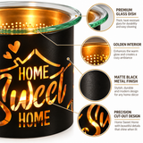 A black metal scented candle holder with a clear glass top and a warm golden-orange interior, featuring the words 'HOME Sweet HOME' in a large cut-out design. The image includes callout circles highlighting the premium glass dish, golden interior, matte black finish, and precision cut-out design.