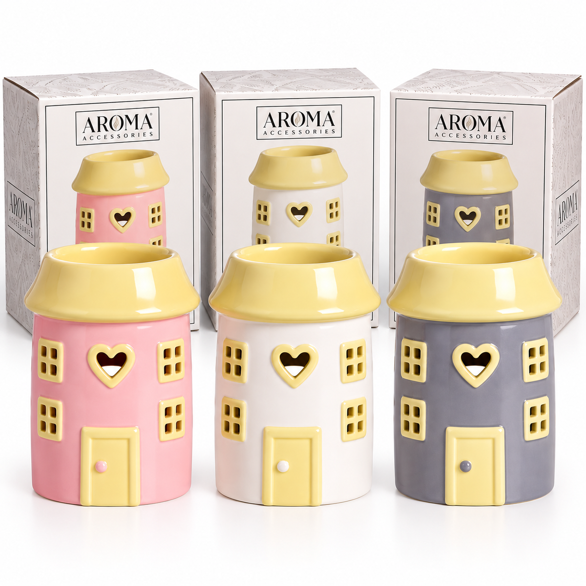 Three small house-shaped ceramic diffusers in pink, white, and gray, each with a yellow roof and heart-shaped window cutout, shown in front of their branded AROMA ACCESSORIES boxes on a white background.