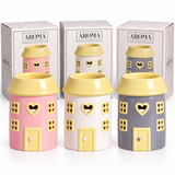 Three small house-shaped ceramic diffusers in pink, white, and gray, each with a yellow roof and heart-shaped window cutout, shown in front of their branded AROMA ACCESSORIES boxes on a white background.