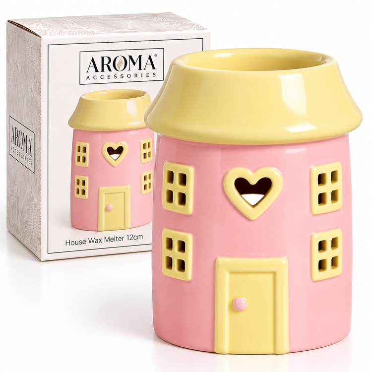 A pink and yellow house-shaped wax warmer with a heart-shaped window and cutout details, shown next to its white AROMA ACCESSORIES retail box.