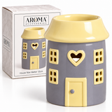 A house-shaped ceramic house wax melter by Aroma Accessories, featuring a gray body and pale yellow roof, windows, door, and heart-shaped cutout, shown next to its product box.