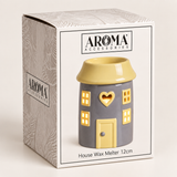 Aroma Accessories house-shaped wax warmer in its retail box. The ceramic house has a gray body, yellow roof, yellow windows, and a yellow door with a heart-shaped cutout.