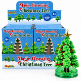 A retail display box of PlayWrite Magic Growing Christmas Trees, shown alongside one assembled green Christmas tree on a clear round base with a gold star topper.