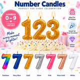 Number 123 glitter birthday candles shaped like the numbers 1, 2, and 3, displayed above a decorated cake. The image shows multiple color options along the bottom: rainbow, navy blue, gold, silver, pink, rose gold, and white.