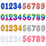 Set of 0-9 birthday candles arranged in rows, showing both glittery and rainbow options in blue, pink, gold, silver, and white on a plain white background.