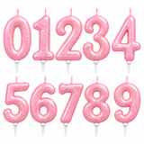 Ten pink glitter number candles spelling out 0123456789, arranged in two rows on a plain white background.