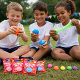 Three children playing with colorful putty and packaging on grass