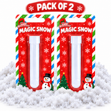 Two packaged tubes of 'Merry Christmas Magic Snow' displayed side-by-side on a bed of white artificial snow, with a red banner at the top reading 'PACK OF 2'.