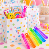 A white polka-dot party favor bag filled with colorful gift items and a pink star-shaped bubble popper, with several rainbow-colored bubble poppers arranged in front on a confetti-covered surface.