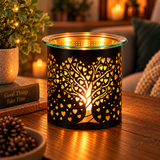 A black metal candle warmer with a glowing tree and heart pattern, set on a wooden table in a cozy living room environment.