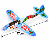 A clear plastic toy airplane decorated with Christmas graphics, including a snowman face on the nose, red 'Merry Christmas' text, a green and red striped scarf, holly, pine trees, and blue sky patterns. Black dimension arrows indicate a length of 17cm on a white background.