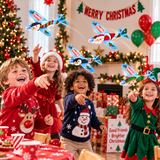 Three children wearing festive Christmas outfits are laughing and pointing at colorful paper airplanes flying in a decorated holiday room with Christmas trees, gifts, balloons, and a 'Merry Christmas' banner.