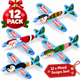 A 12-pack of Christmas airplane ornaments shown on a white background, featuring multiple holiday designs including Santa Claus, an elf, a snowman, a penguin, and green striped patterns. A red ornament badge at the top left says '12 PACK' and a red tag at the bottom right says '12 x Mixed Designs Sent'.