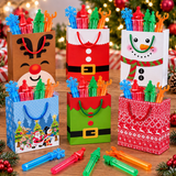 Six Christmas-themed paper gift bags filled with colorful plastic toy syringes, arranged on a wooden surface with holiday decorations and lights in the background.