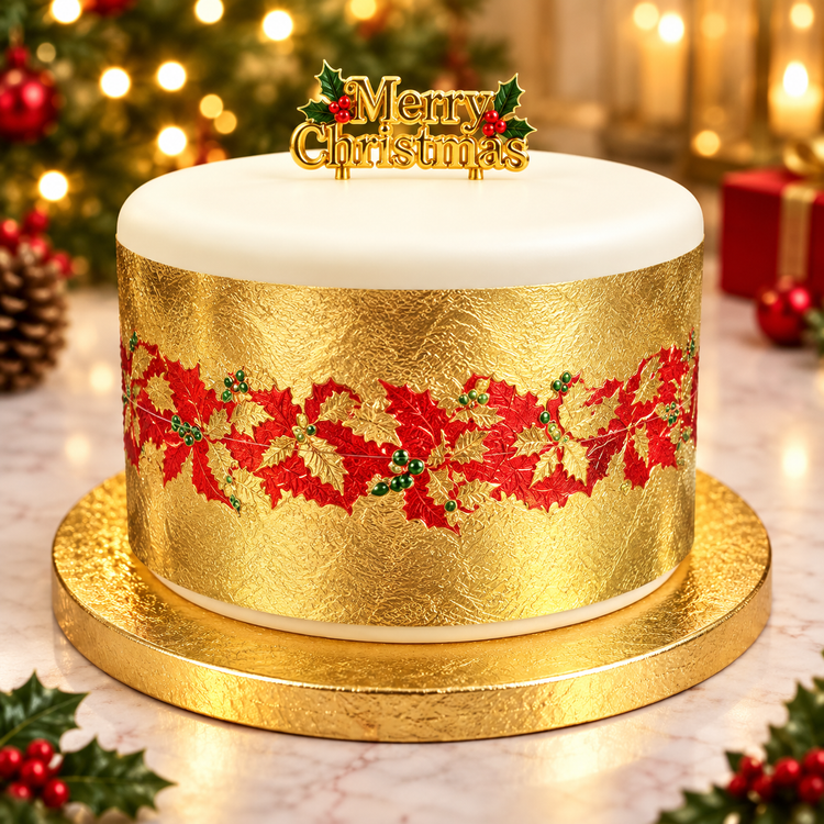 A round Christmas cake with white frosting on top and a textured gold body decorated with a red holly pattern, sitting on a gold cake stand. A gold 'Merry Christmas' topper is placed on top.