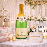 Decorative inflatable bottle labeled 'Celebration' on a wedding gift table with flowers and cards.