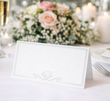 Decorative place card on a table with flowers and candles in the background